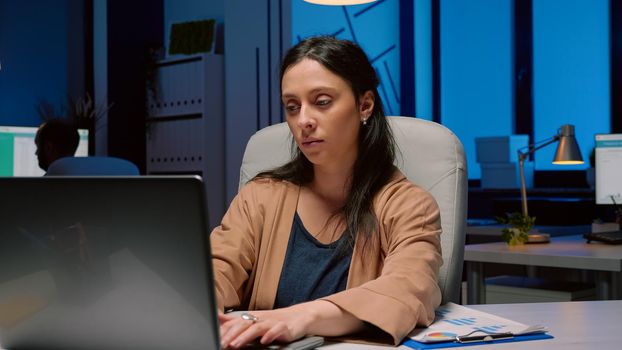 Portrait of tired workaholic entrepreneur analyzing financial statistics using laptop computer working in start-up business company office. Tired overworked businesswoman typing marketing strategy