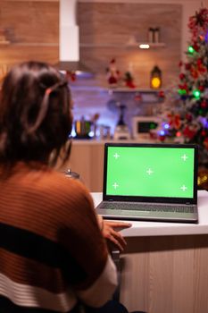 Caucasian adult looking at laptop computer with green screen modern technology for mockup template gadget. Young festive woman using device for digital chroma key isolated display