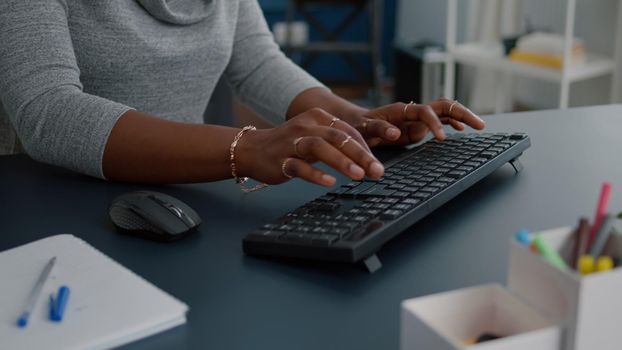 Closeup of african american student hands working at communication project typing information on keyboard using computer sitting at desk in living room. Woman searching business email