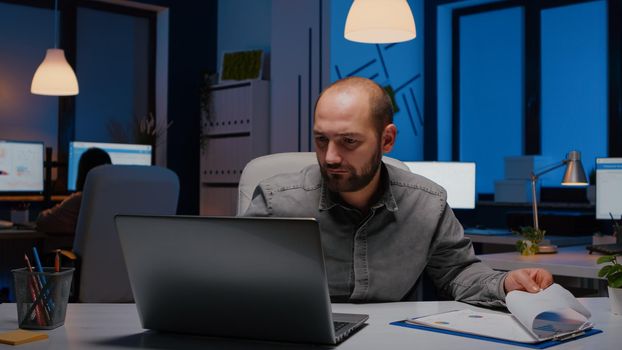 Exhausted workaholic businessman analysing marketing statistics in startup office late at night. Overworked entrepreneur working on financial strategy before company deadline, corporate business management