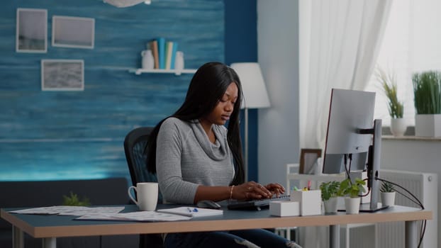 African american student sitting at desk table start typing online homework using computer browsing information on internet searching webinar courses. Black woman working remote from home