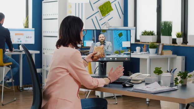 Businesswoman sitting at desk in company office eating sandwich during online videocall conference meeting discussing financial strategy. Takeout order food delivery in corporate job place