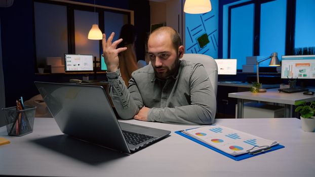 Exhausted businessman discussing marketing deadline project with remote employee during online videocall conference meeting. Entrepreneur sitting at desk table in business company office late at night