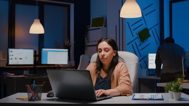 Exhausted workaholic businesswoman yawning while working late at night on laptop before company deadline in startup business office. Stressed overworked frustrated executive manager woman