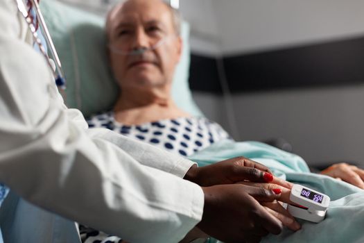 Caring friendly african american doctor therapist holding sick senior patient hand, comforting, showing comapssion, talking about treatment, while he's breathing with help from oxygen mask.