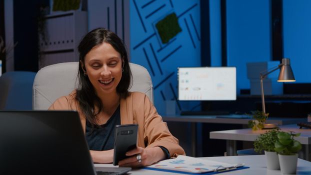 Overworked businesswoman with headphones discussing marketing strategy with teamwork using smartphone. Tired entrepreneur having online videocall financial interview sitting at desk in company office