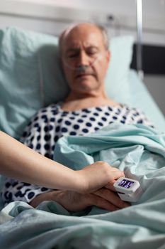 Close up of friendly doctor hands holding patient hand, in hospital room giving encouragement, empathy, support during medical examination. Patient breathing through oxygen mask.