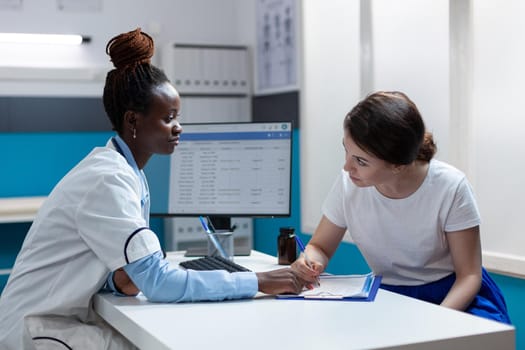 Sick patient signing medical documents discussing medication treatment with african american therapist in hospital office during clinical appointment. Doctor physician explaining disease symptoms