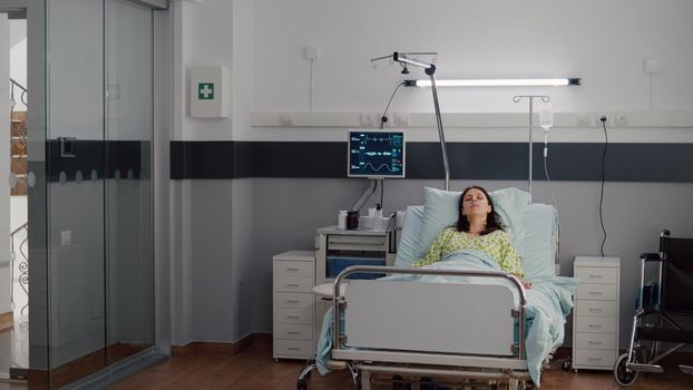 Sick woman wearing nasal oxygen tube resting in bed falling asleep recovering after cardiology procedure. Patient with respiratory disease sitting in hospital ward waiting for medical treatment