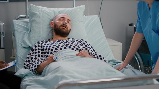 Medical nurse checking temperature monitoring sickness symptom during recovery appointment in hospital ward. Sick man patient resting in bed while assistant analyzing rehabilitation expertise