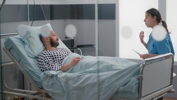 Medical nurse explaining bones radiography to hospitalized sick man during medical recovery analyzing sickness symptom in hospital ward. Patient resting in bed after illness surgery