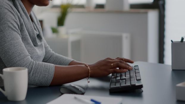 Closeup of african american student hands typing information for communication project using computer sitting at desk in living room. Woman searching business email working remote from home