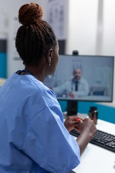 African american practitioner asisstant discussing virus symptom with remote doctor during online videocall meeting conference telework working in hospital office. Telehealthcall on computer screen