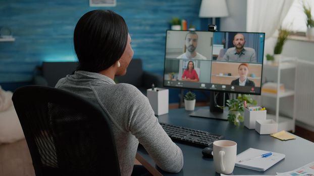 Black student discussing marketing academic ideas with college team having virtual teleconference meeting sitting at desk in living room. Woman working at deadline project during online webinar