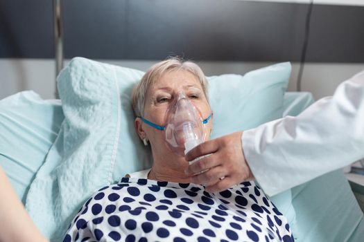 Doctor and nurse supervising senior woman breathing with oxygen mask, laying in bed because of pulmonary disease. Patient laying in bed with iv dip bag attached.