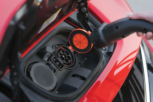 Woman Plugs in Charger into Socket of Her Modern New Red Electric Car. Woman is plugging electric vehicle for charging car battery at parking