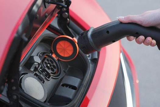 Woman Plugs in Charger into Socket of Her Modern New Red Electric Car. Woman is plugging electric vehicle for charging car battery at parking