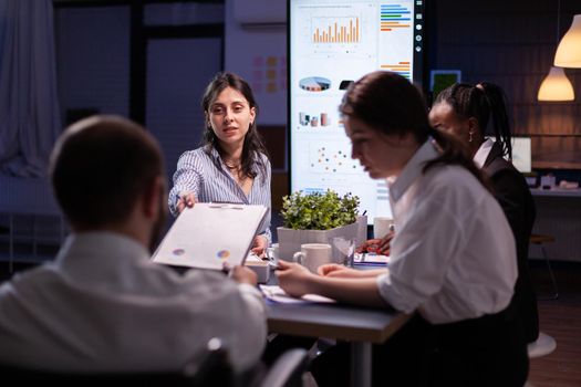 Executive manager woman explaining management statistics working at company strategy overtime in office meeting room. Diverse multi-ethnic businesspeople teamwork brainstorming ideas in evening.