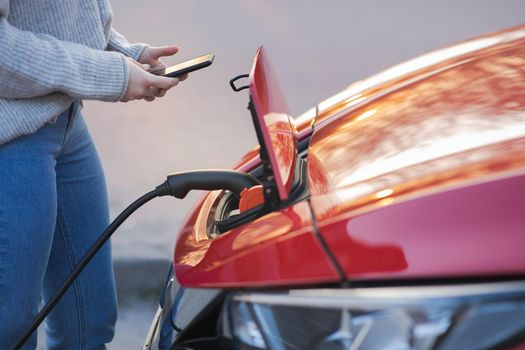 Woman is plugging electric vehicle for charging car battery at parking. Close up. Charging electric car. EV car connected to charger.