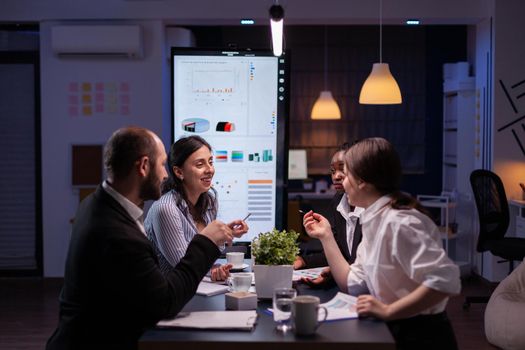 Diverse multi-ethnic businesspeople analyzing management strategy working overtime in company office meeting room late at night. Overworked leader overworking marketing strategy in evening