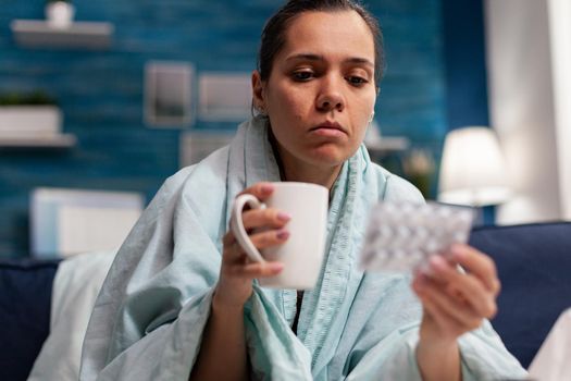 Young sick woman with infection symptoms at home using treatment. Caucasian person with sore throat illness temperature taking medicine pills for cold headache sickness.