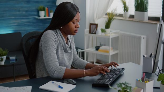 African american student with dark skin working remote from home at marketing online course using webinar university platform. Computer user sitting at desk in living room reading school information