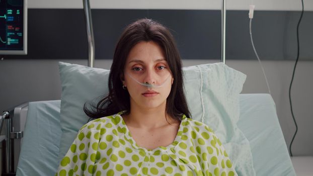 Portrait of sick woman wearing nasal oxygen tube resting in bed recovering after respiratory sickness. Hospitalized patient waiting doctor for medical recovery treatment in hospital ward