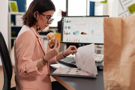 Businesswoman working in startup company office having food meal takeout lunchtime eating tasty sandwich slice typing marketing strategy. Takeaway fastfood order delivered at work place.