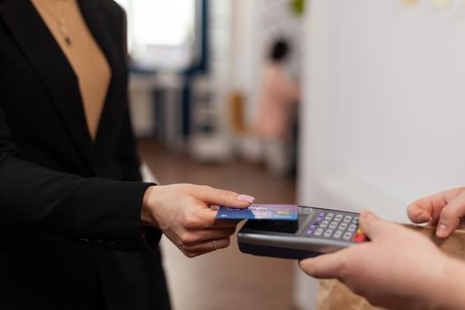 Close up of businesswoman holding plastic credit card in hand, paying for food delivery in company office. Using contactless pay for takeaway food. Bringing tasty meal.