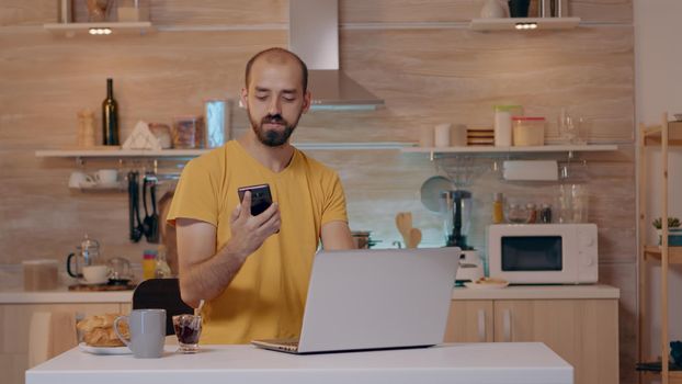 Man working from house with automation lighting system, sitting in kitchen switch off the lights using voice command to smart home application on smartphone. Person controlling light with wifi gadget