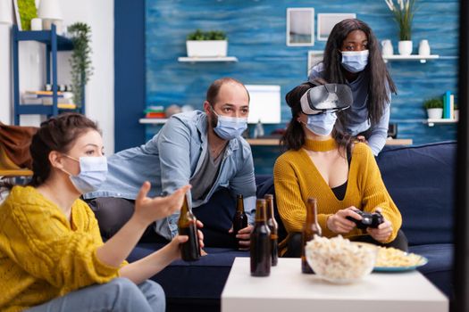 Mixed raced friends in home living room having a video game competion keeping social distancing wearing face mask to prevent sickness with covid. Experiencing virtual reality. Conceptual image.