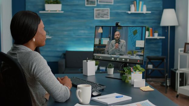 Smart black student working at marketing deadline project discussing academic ideas with entrepreneur during online videocall teleconference meeting. Woman sitting at desk using high school webinar