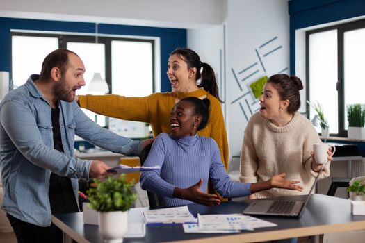 African manager businesswoman and diverse team celebrating victory after closing deal with important client. Multiethnic business team with laptop and papers excited about project.