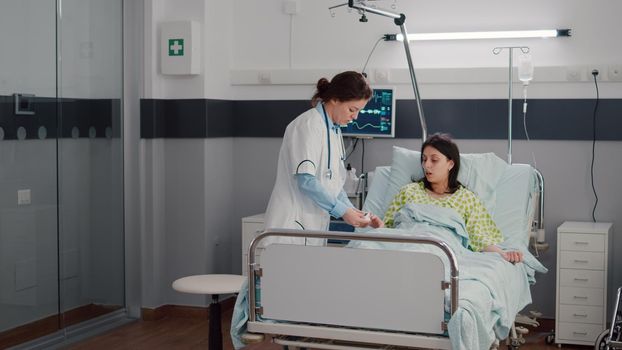 Woman doctor monitoring sick woman during rehabilitation appointment in hospital ward putting oximeter checking sickness expertise. Patient resting in bed waiting disease treatment