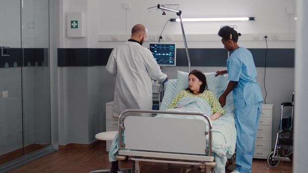 Afro american nurse arrange sick woman bed during medical recovery working in hospital ward, Practitioner doctor checking patient monitoring disease diagnosis explaining rehabilitation treatment