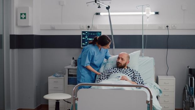 Woman practitioner assistant checking sick man monitoring heartrate pulse using oximeter during medical appointment. Patient resting in bed having respiratory disorder waiting recovery treatment