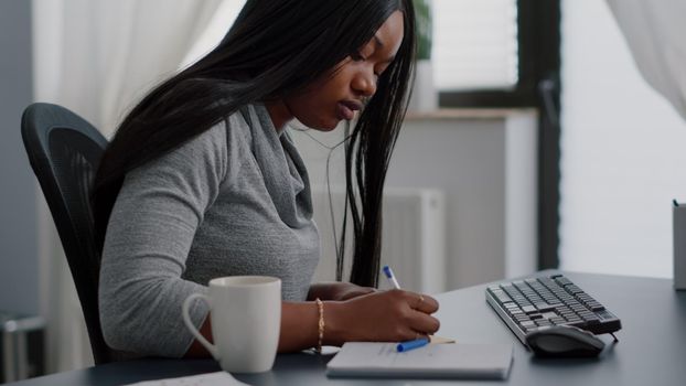 African american student writing univeristy information on stickey notes putting on computer typing school homework using elearning platform during online course. Black woman working remote from home