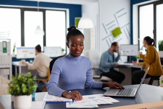 African in marketing corporate office working to finish deadline, checking charts. Diverse team of business people analyzing company financial reports from computer.