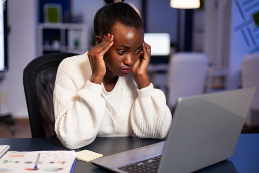Overworked black businesswoman looking worried at laptop rubbing temples. Stressed employee using modern technology doing overtime for deadline of project.