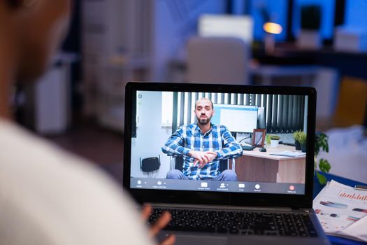 African businesswoman having corporate meeting with remotely paralyzed man using webcam of laptop sitting in start up business office working overtime. Manager talking on video conference at midnight.