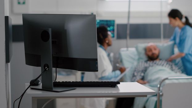 Practitioner doctor with black skin explaining disease treatment with sick man writing medical recovery on clipboard while nurse arrange bed. Hospitalized patient having respiratory disorder