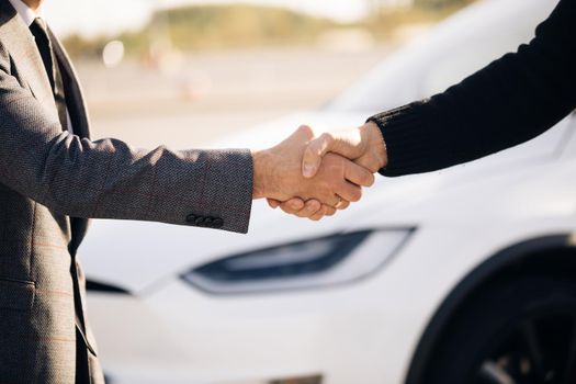 Male hand gives a car keys to male hand in the car dealership close up. Unrecognized auto seller and a man who bought a vehicle shake hands. Dealer giving key to new owner in auto show or salon.
