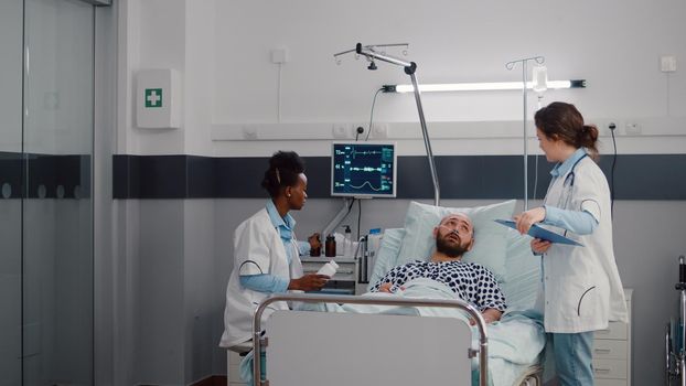 Afro american physician doctor discussing pills treatment against illness during medical appointment in hospital ward. Sick man patient with oxygen tube resting in bed explaining pain symptom