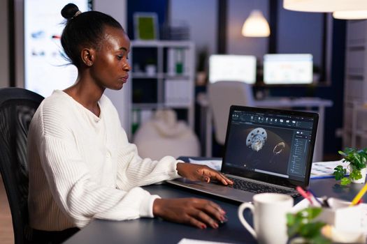 African woman engineer working at new project using laptop doing overtime at night sitting at desk in start-up office. Industrial construction designer studying on pc showing cad software in midnight.