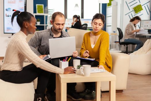 Group of diverse startup company colleague entrepreneur sitting on couch in professional workplace, brifing and sharing ideeas over financial strategy management. Employees working together at office.