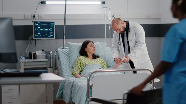 Therapist doctor analyzing heart pulse during medical consulting in hospital ward. Afro-american nurse putting sick patient in wheelchair for physiotherapy recovery for leg accident