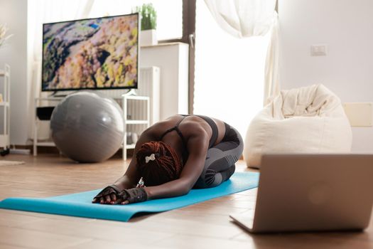 African black fit woman dressed in sportwear relaxing on yoga mat, watching online training exercise using laptop in home living room for wellbeing, Workout and healthy lifestyle.