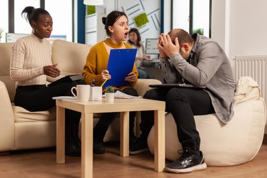 Angry manager woman arguing disagreeing about bad business contract, diverse colleagues having conflict dispute about document sitting on couch at office desk, partners shouting breaking agreement.