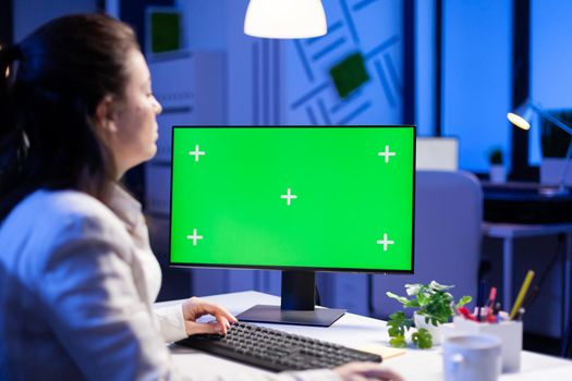 Businesswoman looking at green screen monitor of computer sitting at desk during online web conference. Freelancer watching desktop monitor display with green mockup, chroma key in business office