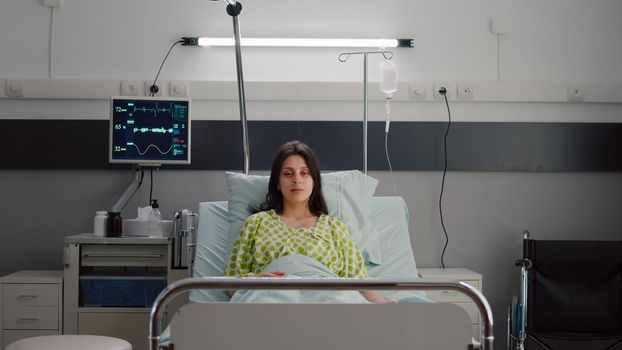 Patient wearing with nasal oxygen tube looking into camera sitting in bed during online videocall conference. Sick woman with breathing disease waiting for illness treatment in hospital ward